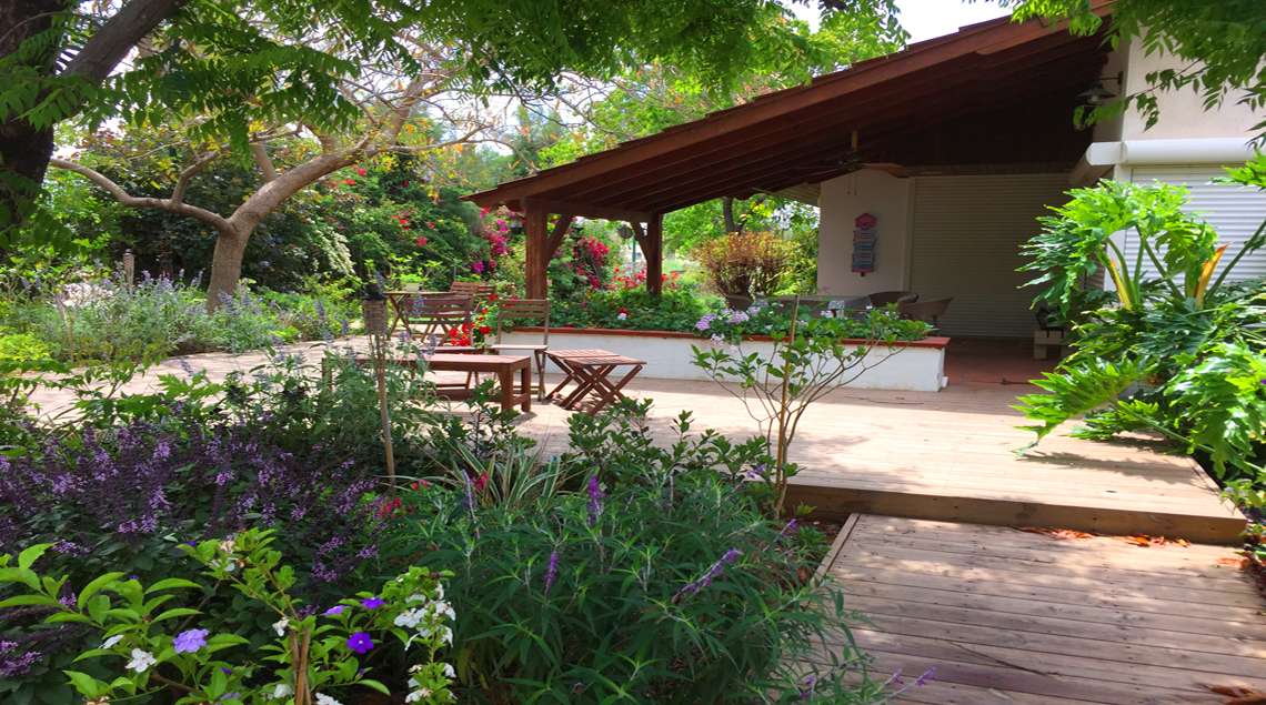 פינת ישיבה מוצלת על דק עם צמחים פורחים מסביב בגוונים של סגול.