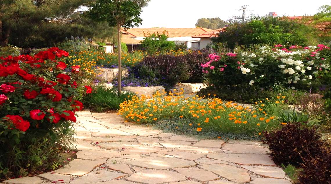 שביל אבני מדרך ובתוכו משולבות ערוגות פורחות בכתום, אדום, לבן וורוד.