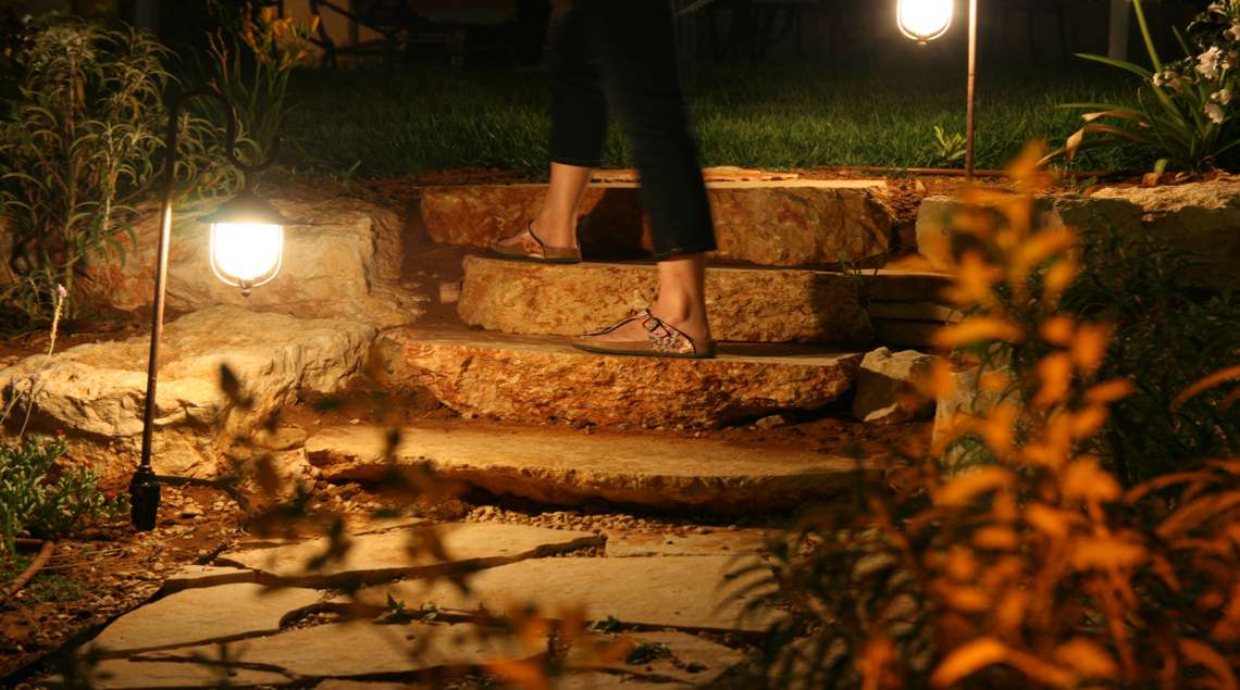 תאורת גינה בלילה לאורך מדרגות סלע שעליהן מטפסת אשה.