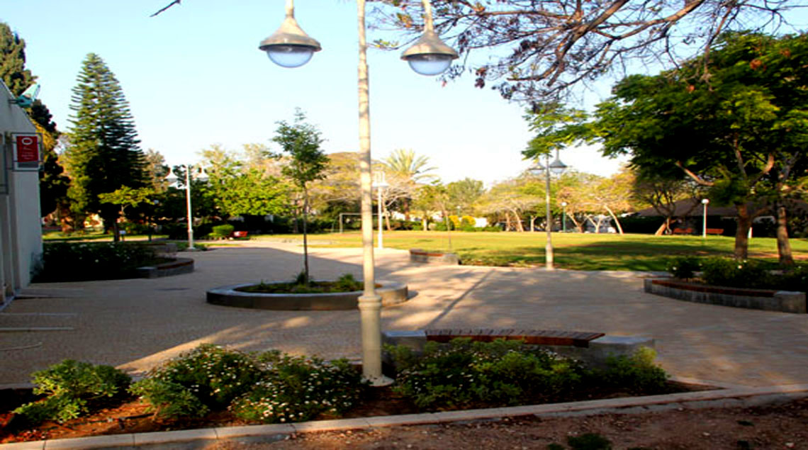 ערוגה ירוקה, עמודת תאורה בצבע קרם וספסל ישיבה עגול מבטון שתוחם ערוגה ירוקה.