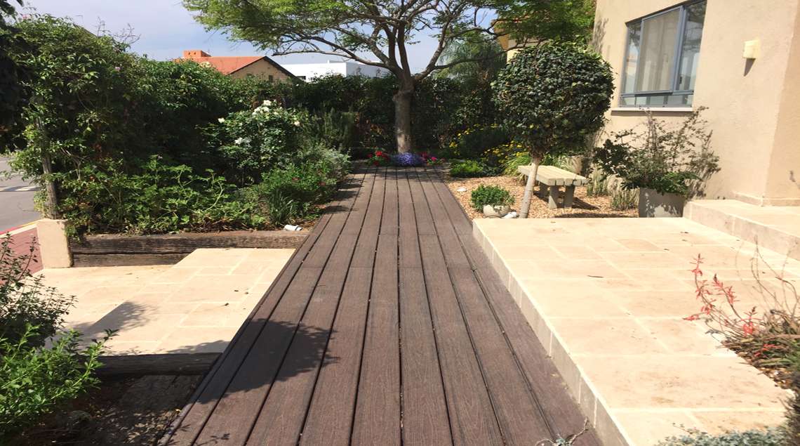 שביל דק בתוך מדרגות אבן שמסתיים בערוגה פורח תחת עץ צל גדול