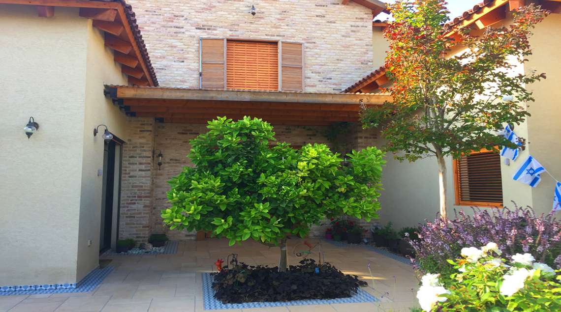 פאטיו כניסה לבית שבמרכזו ערוגה תחומה באריחים מצוירים בצבע תכלת ובתוכה שתול עץ פומלה.