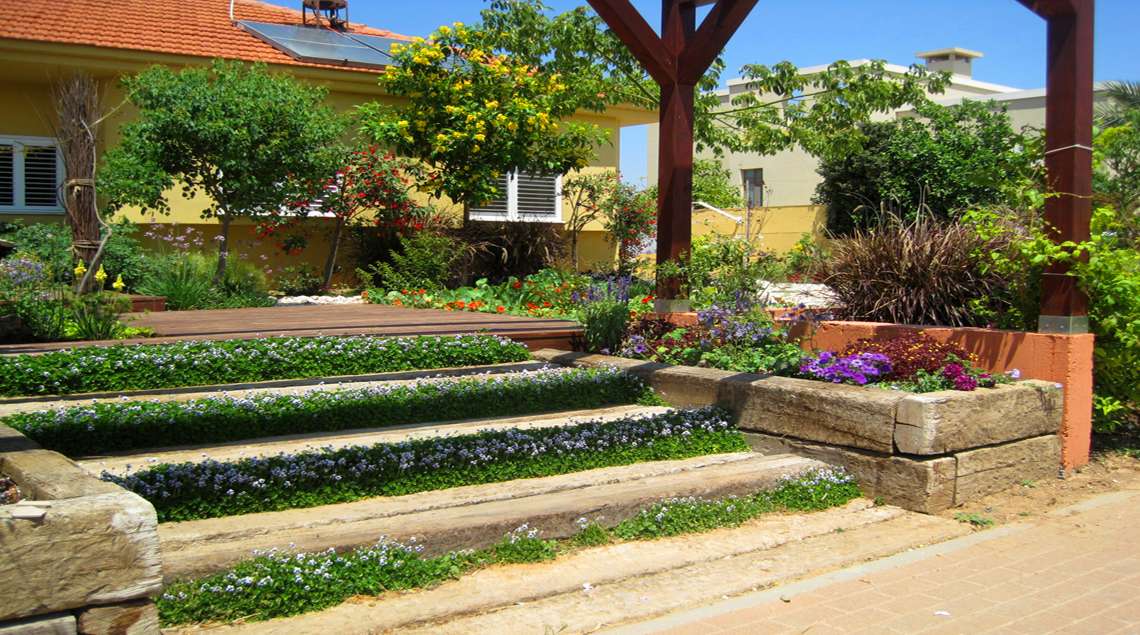 מדרגות וערוגות מאדני רכבת. בין אדנים שתולה סיגלית אוסטרלית עם פרחים קטנטנים בגוון של לבן עם סגול.