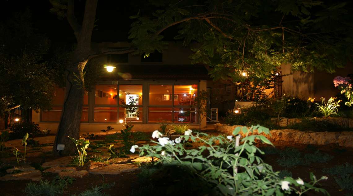 תאורת לילה בגינה על רקע חלונות גדולים של סטודיו למחול שפונה לגינה.