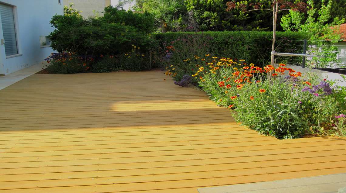 דק עץ ולצידו ערוגה פורחת בכתום וצהוב.