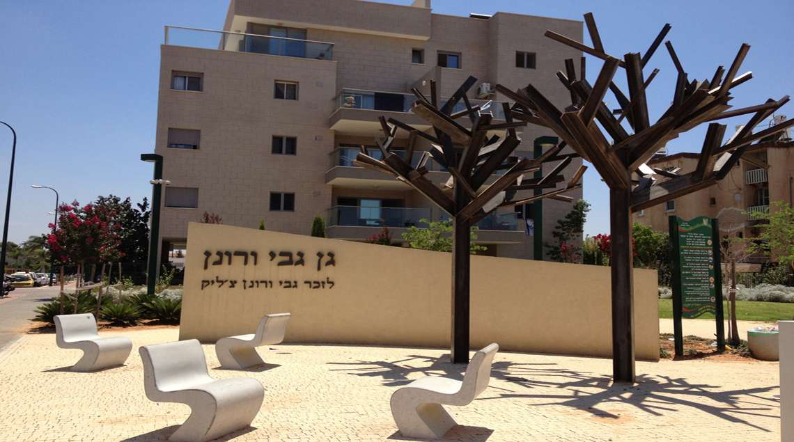 קיר ההנצחה, עליו רשומים שמות האחים גבי ורונן צ'ליק. הפסל של שני העצים. ומקדימה כסאות הבטון.