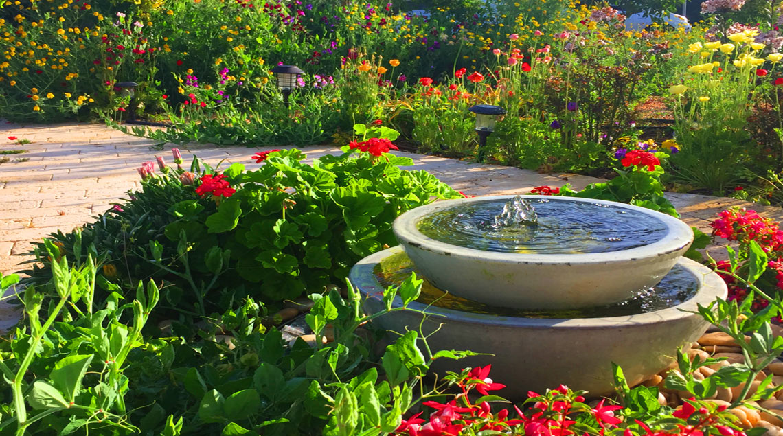 אלמנט מים של שתי קערות קרמיקה בצבע קרם מונחות אחת על השנייה. על רקע גינה פורחת