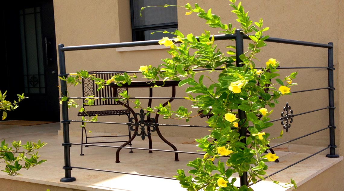 פינת ישיבה אינטימית בכניסה לבית, תחומה במעקה ברזל עם מטפס צהוב שמשתרג עליו.